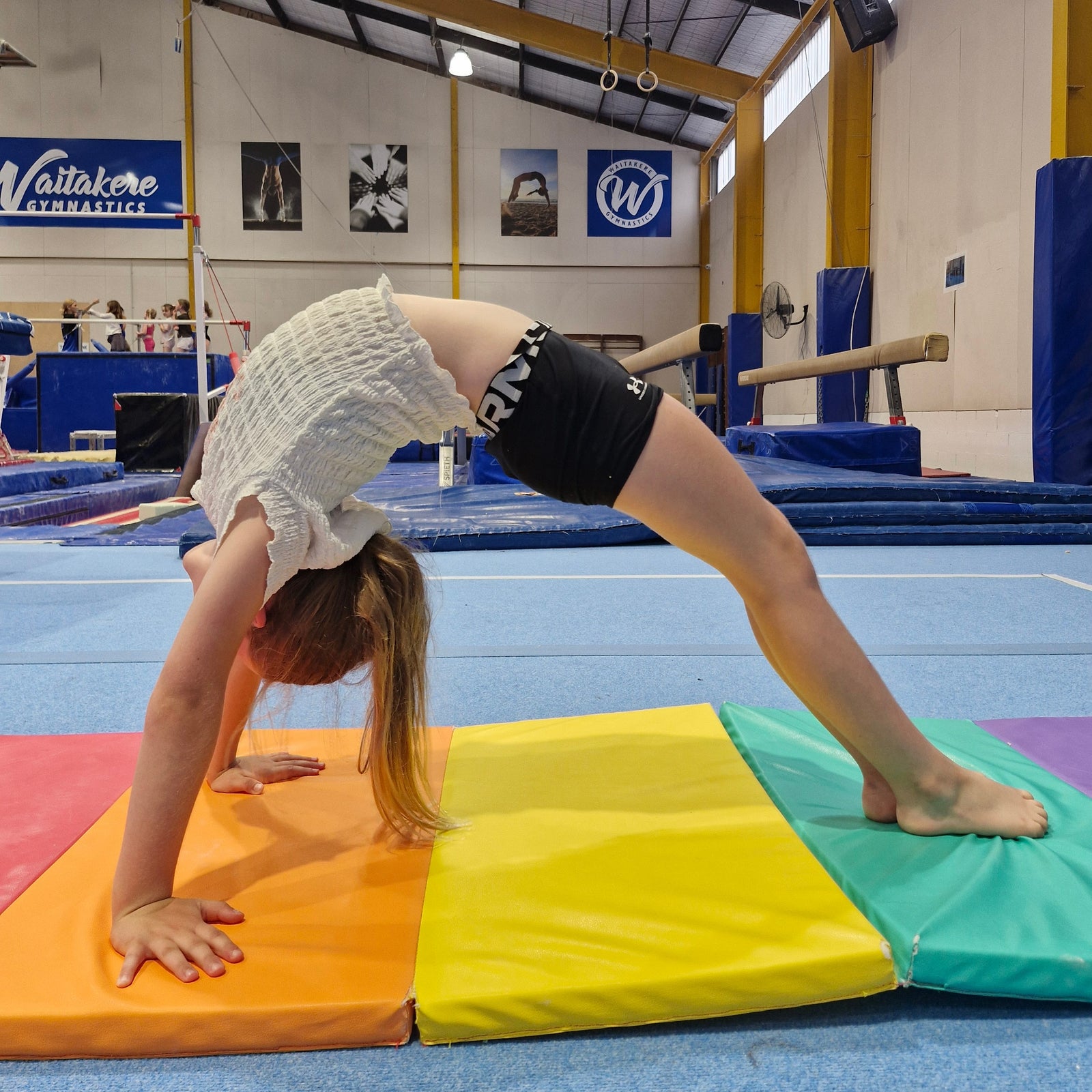 Girl performing bridge on rainbow mat during gymnastics class