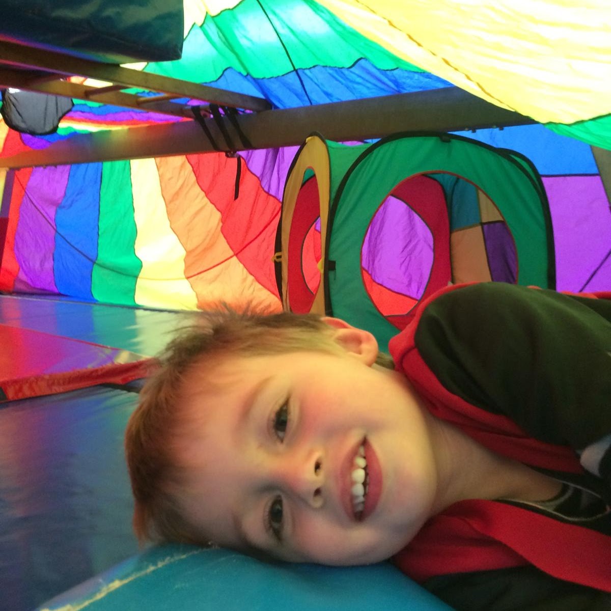 Young child lying under colourful parachute during springboard mini gymnastics class