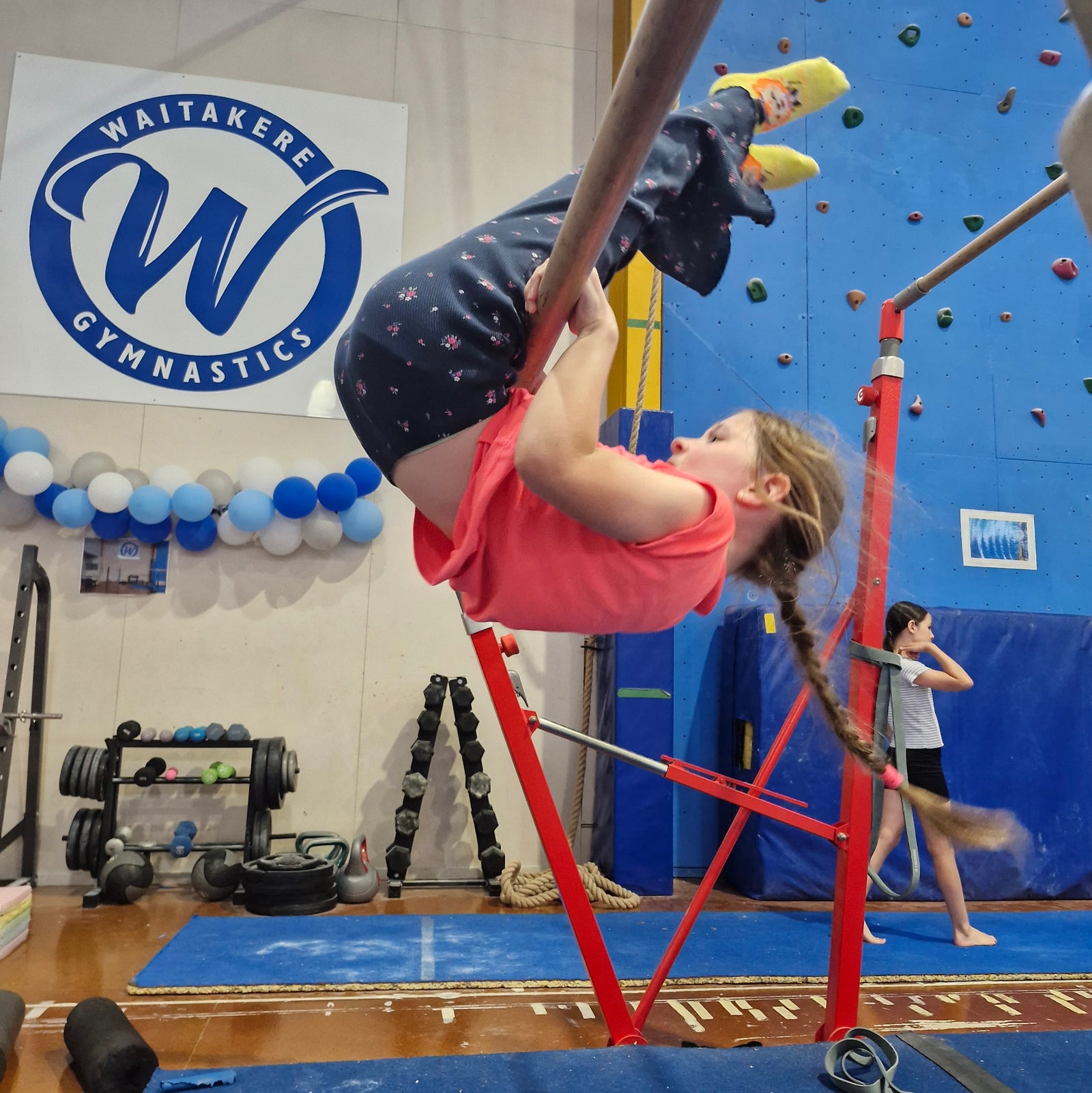 Girl wearing pink shirt doing a circle over on low bar during gymnastics